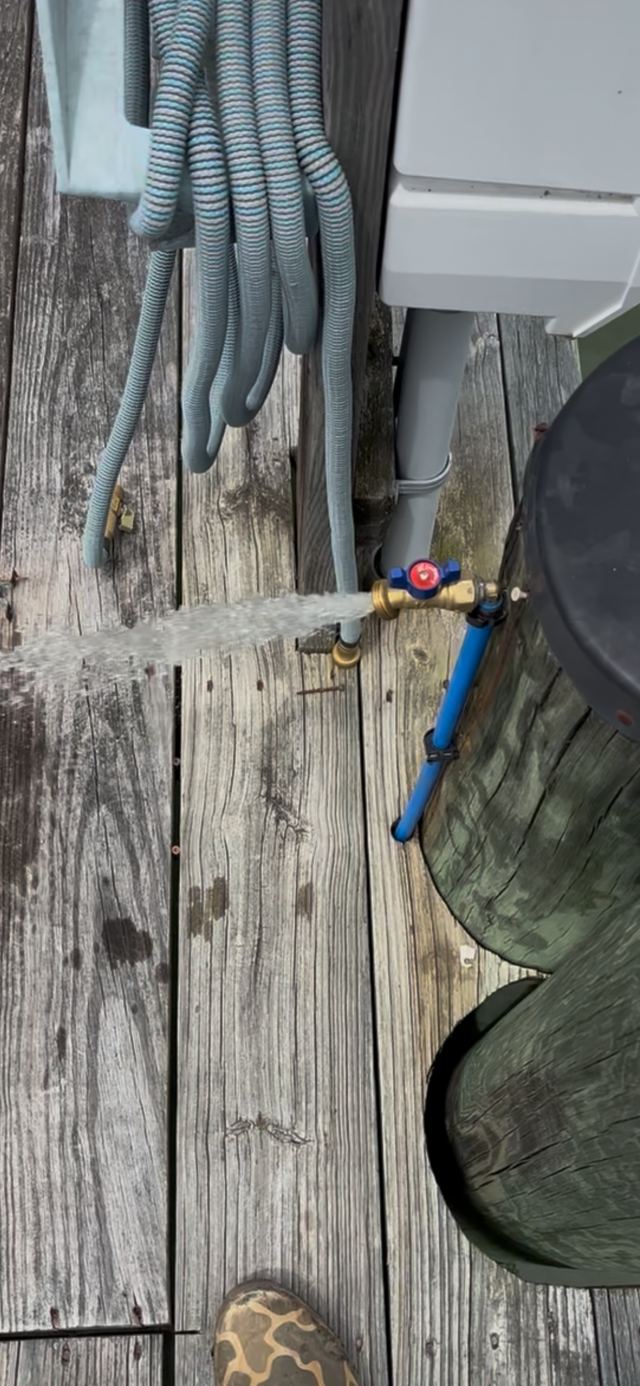 Outdoor hose bib with a red handle running water on a wooden deck